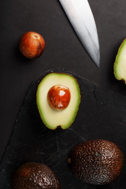 Фото Нарезанный целиком органический авокадо хасс ножом на черной поверхности. источник незаменимых жиров, витаминов, микроэлементов, бета-каротина и жирных кислот омега-3.