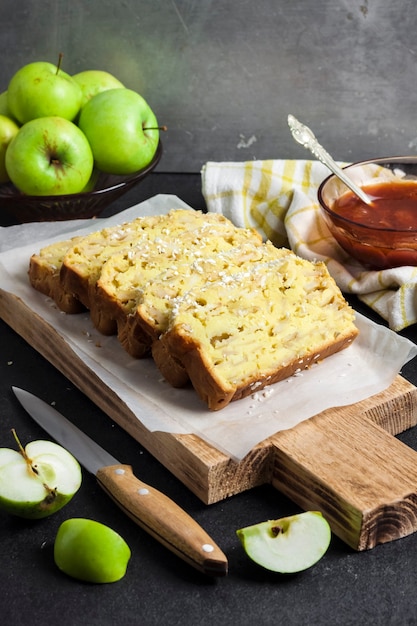 Sliced apple and coconut oaf cake on wooden cutting board on dark background