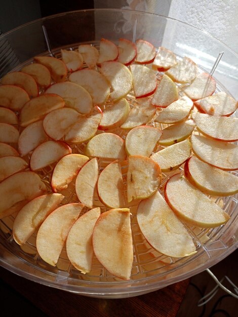 Foto le mele tagliate sono disposte in un asciugatore elettrico nella casa vicino alla finestra preparando frutta secca per l'inverno foto verticale in primo piano