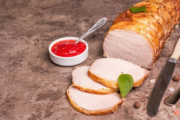 Sliced baked pork loin on a stone concrete background. A trendy hard light, dark shadow, spices and herbs, close up