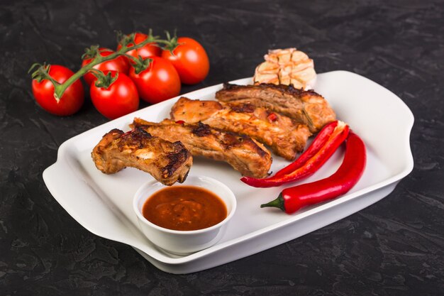 Sliced baked pork ribs on a white plate with hot pepper and red sauce and tomatoes