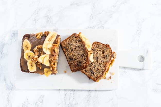 Sliced banana nut bread drizzled homemade caramel on a marble cutting board.