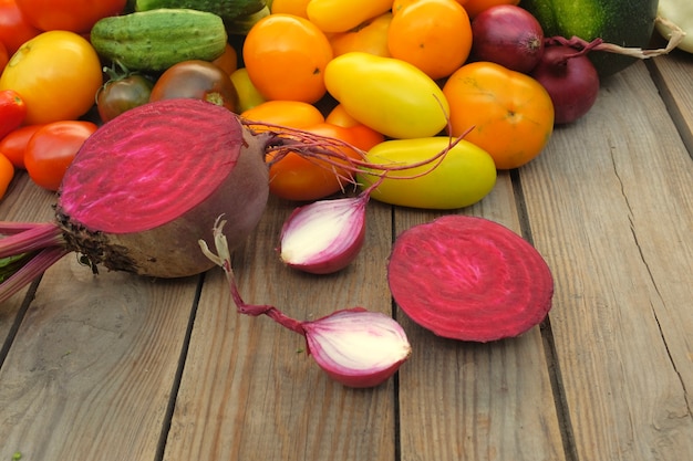 Sliced beets and onions lie on a wooden board against a background of different bright vegetables. Harvest and cooking concept.