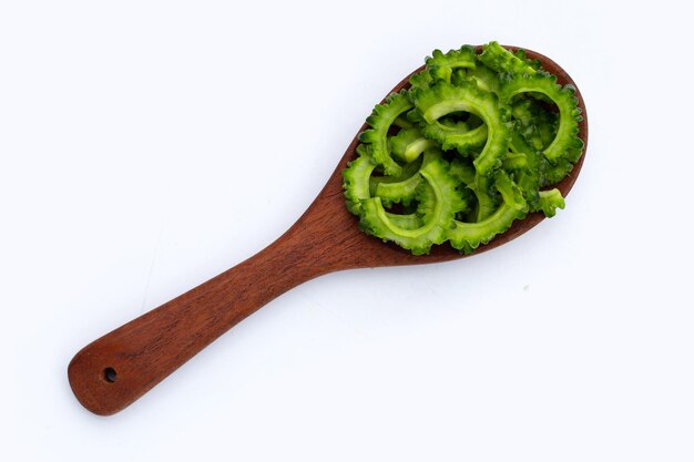 Sliced bitter gourd in wooden spoon on white background.