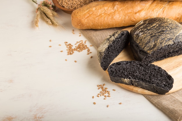 Sliced black bread with different kinds of fresh baked bread on a white wooden background. side view, copy space.