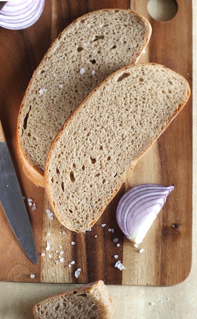 Sliced bread lies on a wooden board There is an onion nearby Salt is scattered on the board