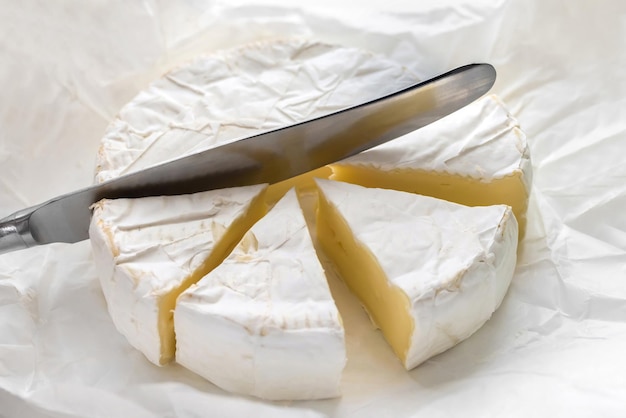 Нарезанный сыр бри и кухонный нож на белой крафт-бумаге
