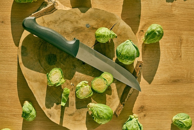 Photo sliced brussels sprouts and a chefs knife on a wooden kitchen counter.