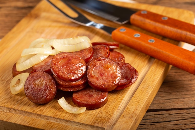 Sliced calabrese sausage with onion on wooden background