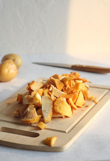 Sliced chanterelle mushrooms lie on a wooden board on the table Behind lies a potato