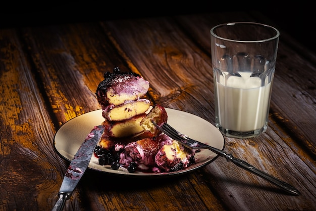 Sliced cheesecakes with blueberry jam and sour cream on a plate with a glass of milk on the table