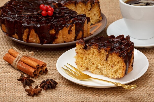Нарезанный шоколадный торт, украшенный пучком калины, чашкой кофе, звездчатым анисом и корицей на столе с мешковиной