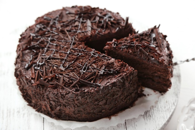 Sliced chocolate cake on wooden table on light background