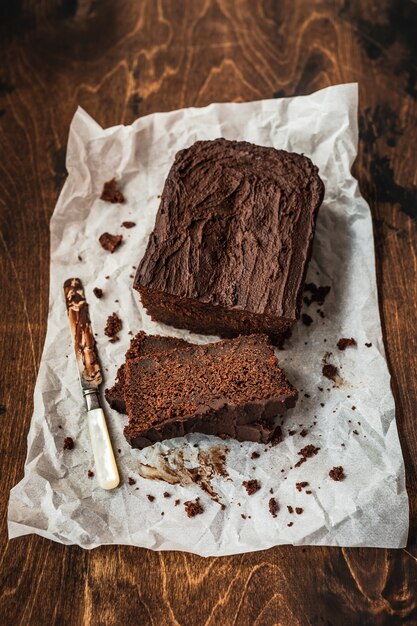 Sliced chocolate loaf cake and a knife on baking paper on dark wooden table