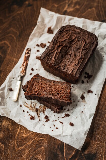 Sliced chocolate loaf cake and a knife on baking paper on dark wooden table