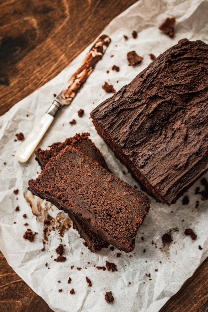 Sliced chocolate loaf cake and a knife on baking paper on dark wooden table