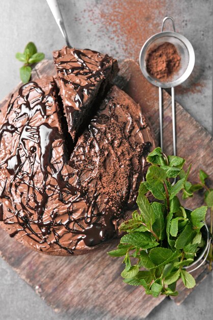 Photo sliced chocolate pie with pile of mint and sieve on cutting board