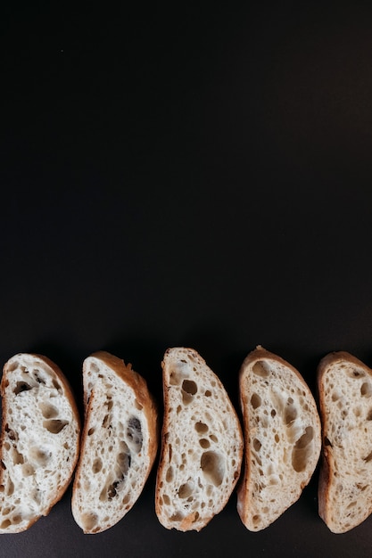 Fette di pane ciabatta su sfondo nero. pane bianco italiano. vista dall'alto con copia spazio.