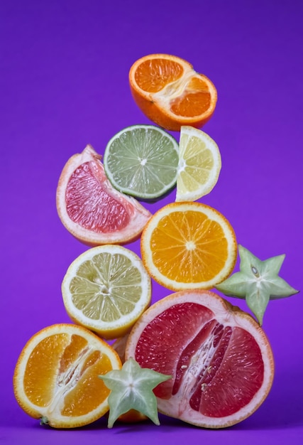 Sliced citrus fruits in different sizes and colors close up on purple background