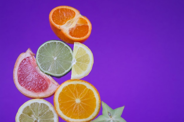 Sliced citrus fruits in different sizes and colors close up on purple background