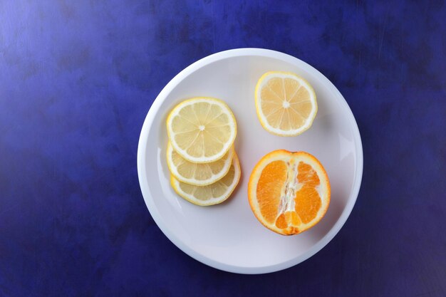 Sliced citrus fruits on a white plate on a blue background Healthy eating and food concept Citrus fruits arrangement Closeup