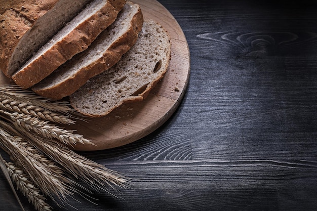 Sliced crusty bread on wooden carving board golden wheat rye ears