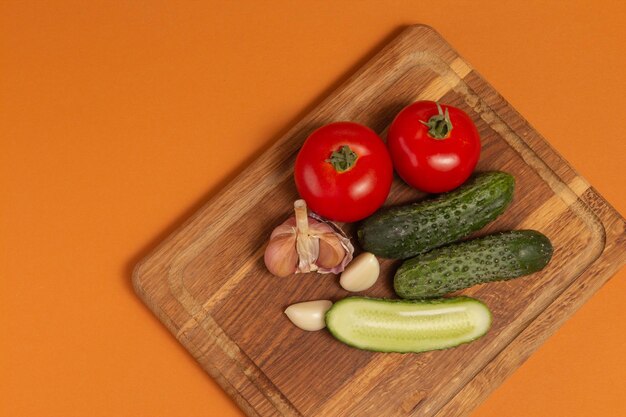 Sliced cucumber tomatoes and garlic on wooden cutting board Tomatoes with green ponytails