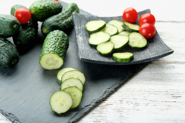 Sliced cucumbers with tomatoes on black plank on wooden background