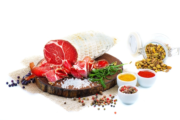 Sliced cured coppa with spices and a sprig of rosemary. Isolated on white.