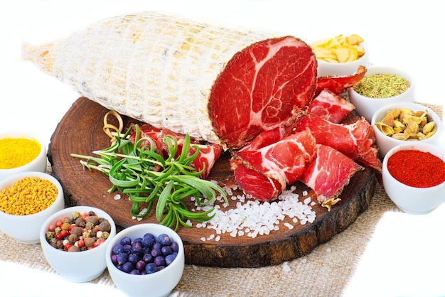 Sliced cured coppa with spices and a sprig of rosemary. Isolated on white.