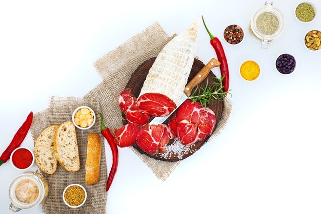 Sliced cured coppa with spices and a sprig of rosemary. Isolated on white.