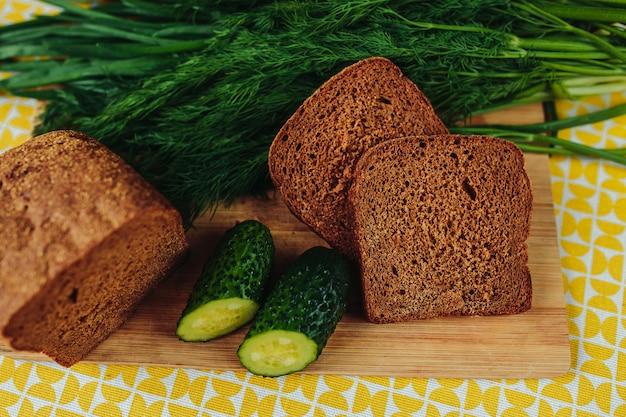 Sliced dark bread on wooden cutting board with sliced cucumbers. Healthy nutrition, healthy food on the table, greens, cucumbers and dark bread.