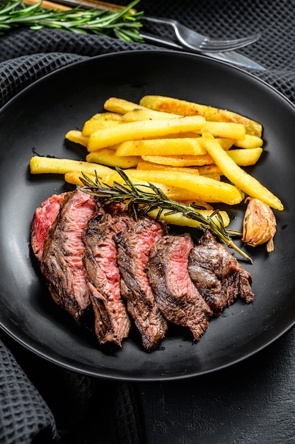 Sliced Flat Iron steak with French fries, marbled meat. Black background. Top view