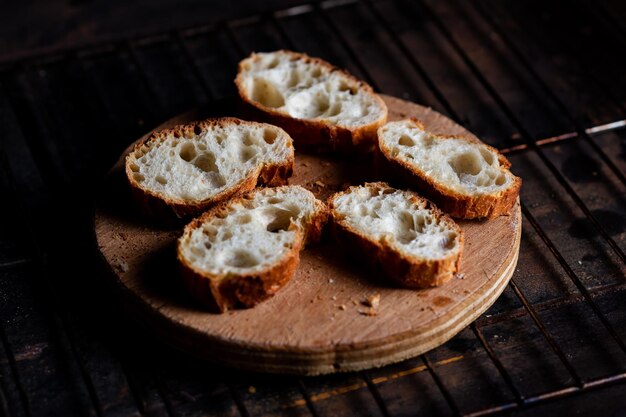 Sliced French baguette on a wooden board on a dark background Bread with big holes Preparing for bruschetta