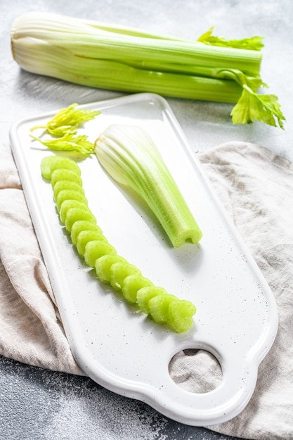 Sliced fresh celery stalk on cutting white board. Gray background. Top view