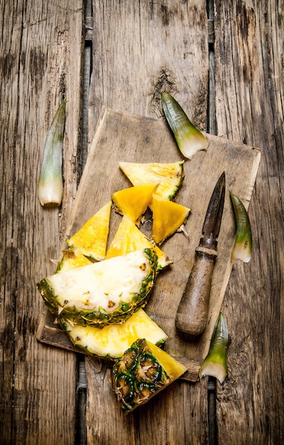 Foto ananas fresco a fette con un coltello sul tagliere sulla tavola di legno. vista dall'alto