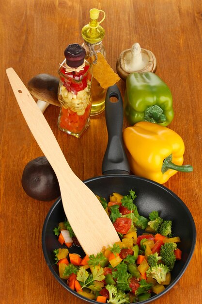 Sliced fresh vegetables in pan with spices and ingredients on wooden table