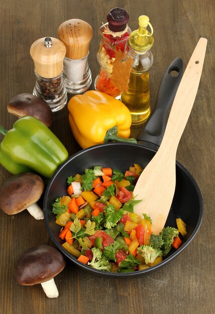 Sliced fresh vegetables in pan with spices and ingredients on wooden table