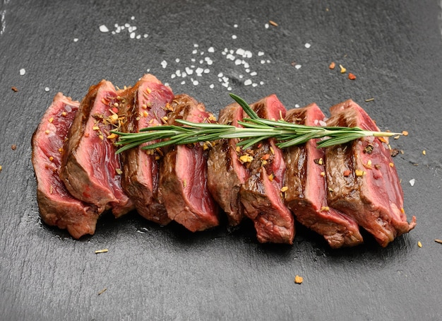 Sliced fried beef steak New York  striploin on a black surface with spices, degree of doneness rare, close up