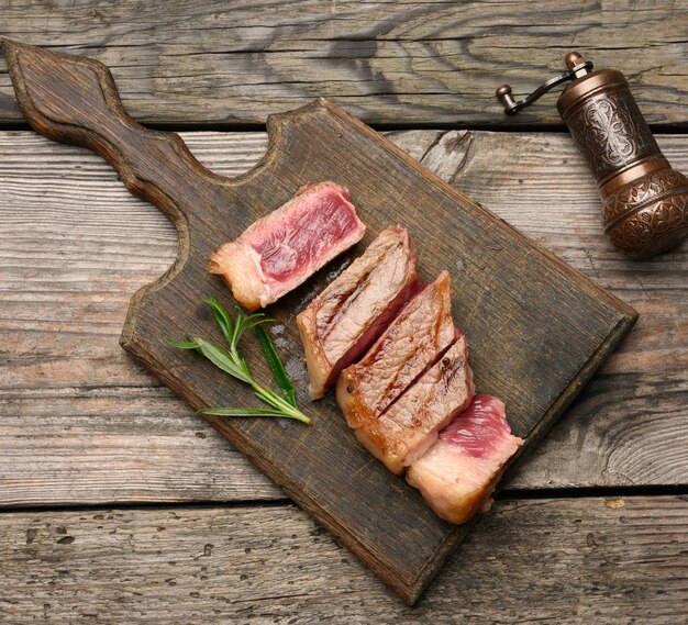 Sliced fried beef steak New York striploin on a wooden cutting board, degree of doneness rare, top view