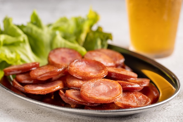 Sliced fried pepperoni sausage with glass of beer on the table