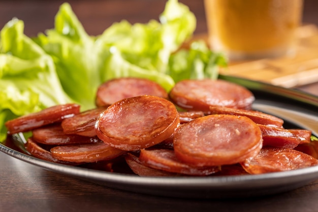 sliced fried pepperoni sausage with glass of beer on the table