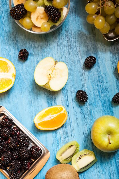 Sliced fruits and barries over a blue desk in studio. Natural refreshment tropical nutrition