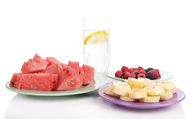 Sliced fruits and berries on plate with glass of water isolated on white