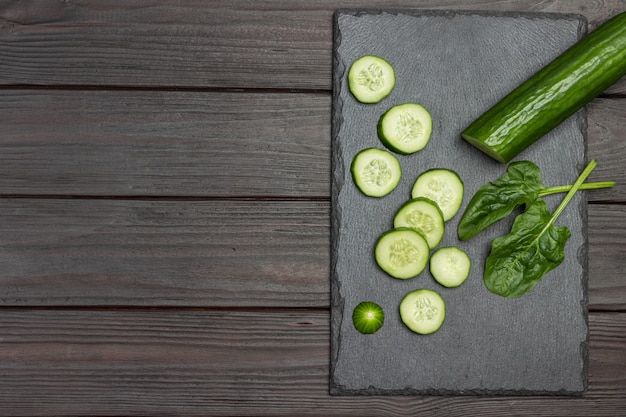 Sliced green cucumber on black cutting board. Wooden background. Flat lay. Copy space