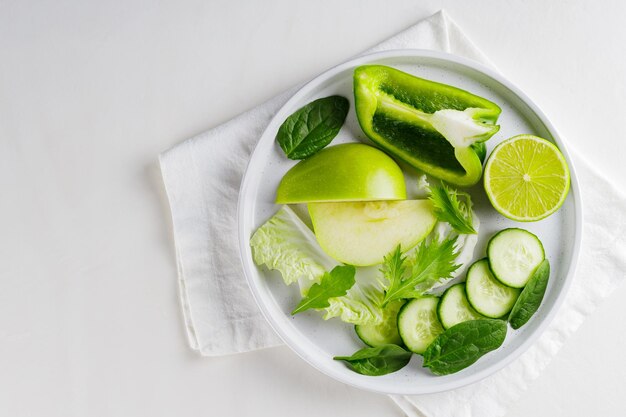 白い皿に緑の野菜と果物をスライスしました。白い背景の上の新鮮な緑のダイエット食品。スペースをコピーします。上面図