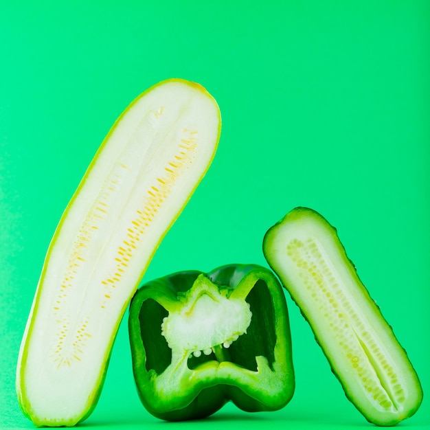 緑の壁に緑の野菜をスライスしました。ビーガン用のピーマン、キュウリ、ズッキーニ。健康食品のコンセプト。落ちてくる野菜