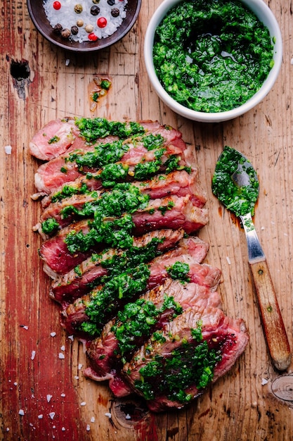 Нарезанный стейк из говядины на гриле с зеленым соусом чимичурри на деревянном фоне