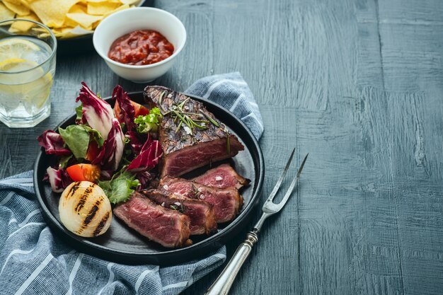 Barbecue arrostito affettato del manzo con insalata fresca e la cipolla fritta sopra fondo blu