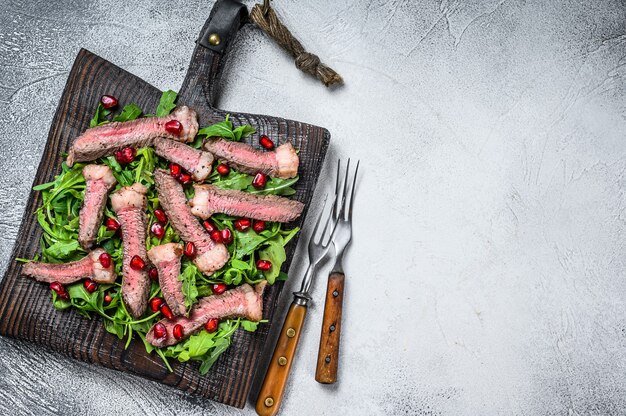 Fette di bistecca di manzo alla griglia con insalata di foglie di rucola sul tagliere rustico